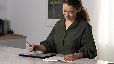 A person using a tablet with a pen while looking at a notebook.