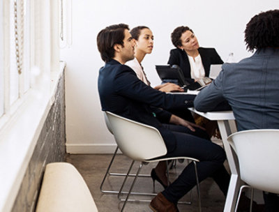 Four people sitting at a table in a conference room listening to someone who is out of frame