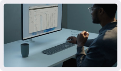 Person working at a desk using a computer monitor displaying a data table.