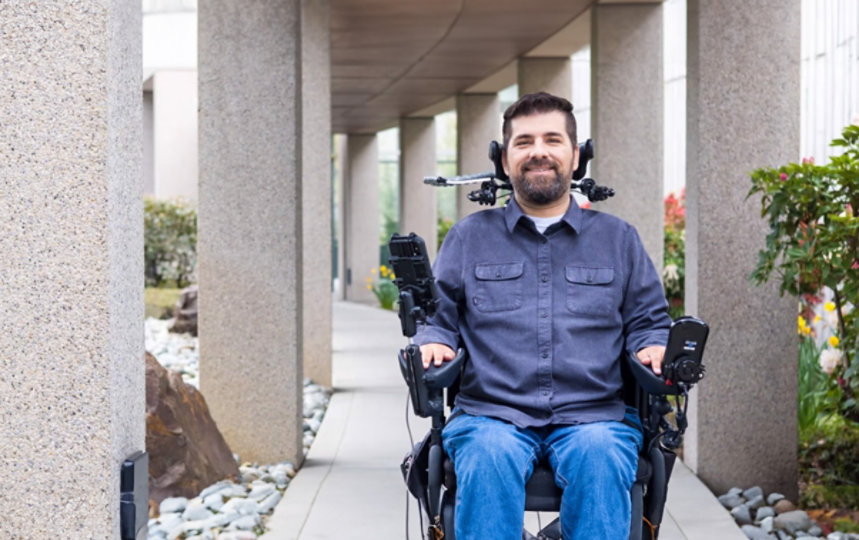 A man in a wheelchair with computer monitors behind him