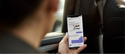 Person in a car holding a smartphone, viewing a chat conversation on the screen.