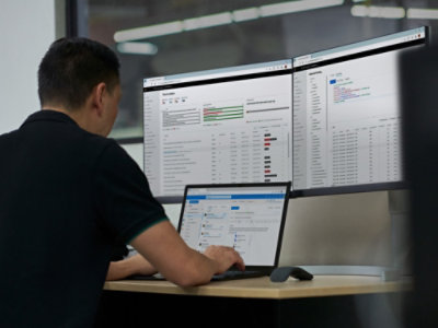 A person working on a laptop with computer monitors in view.