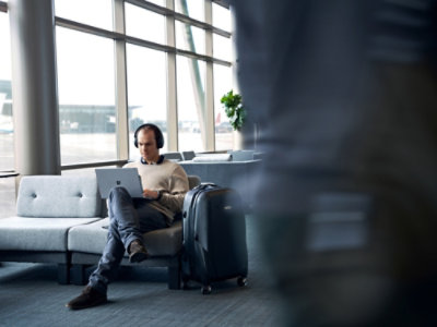 Person seated in an airport lounge using a laptop, with a suitcase nearby.