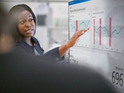 A person pointing at a graph on a transparent board with numbers 130 and 696 visible.