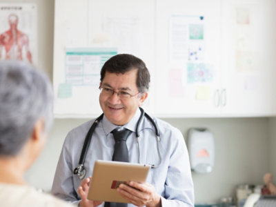 A doctor holding a tablet while interacting with a patient.