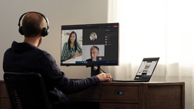 A person sitting at a desk with a laptop and monitor and participating in a Teams video call