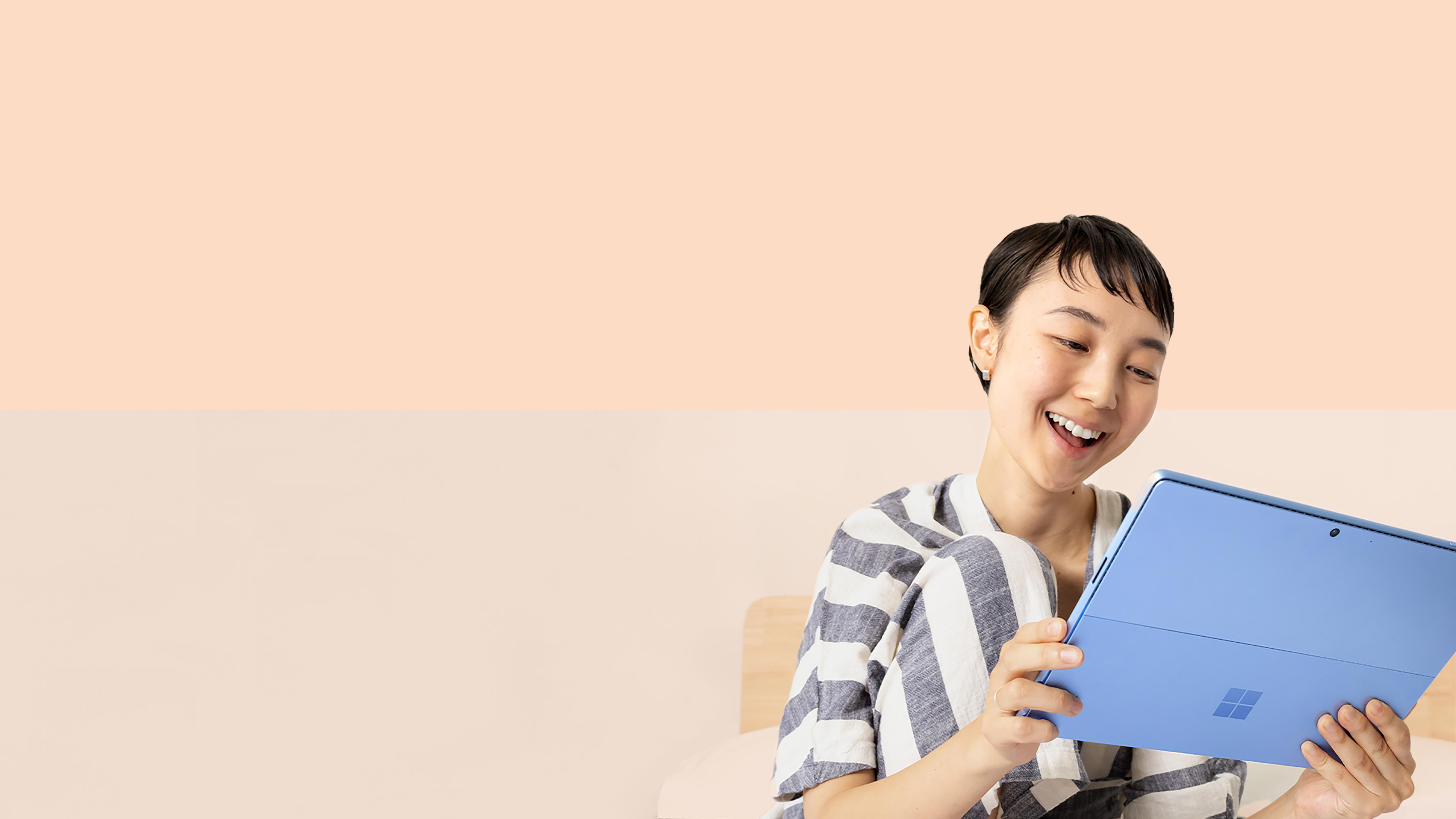 Een vrouw glimlacht naar haar Surface Pro 9 in Sapphire terwijl ze een Surface Slim Pen 2 vasthoudt.