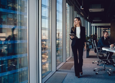Personne marchant dans un bureau devant un mur vitré et tenant une tablette