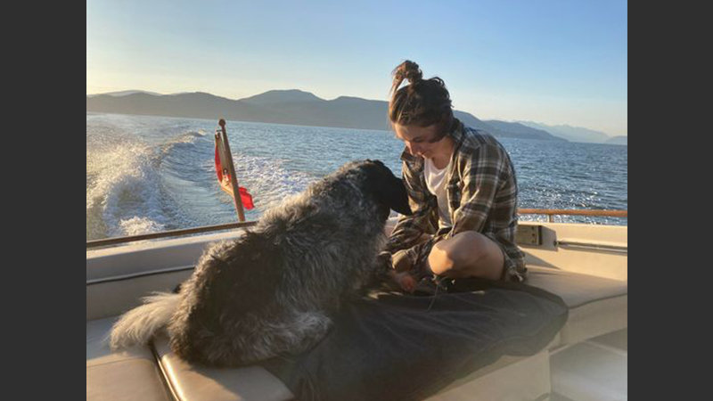 Kiah McGeer and her dog  sitting on the back of a boat, enjoying the calm sea during sunset