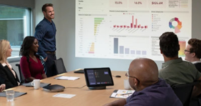 Fotografi med en person som håller en presentation för människor i mötesrummet och online