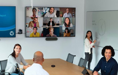 Vier Personen in einer Besprechung, während weitere Teilnehmende über eine Teams-Videounterhaltung auf einem großen Raumdisplay zugeschaltet sind