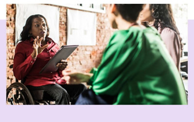 Personne en fauteuil roulant tenant une tablette et parlant à deux collègues.