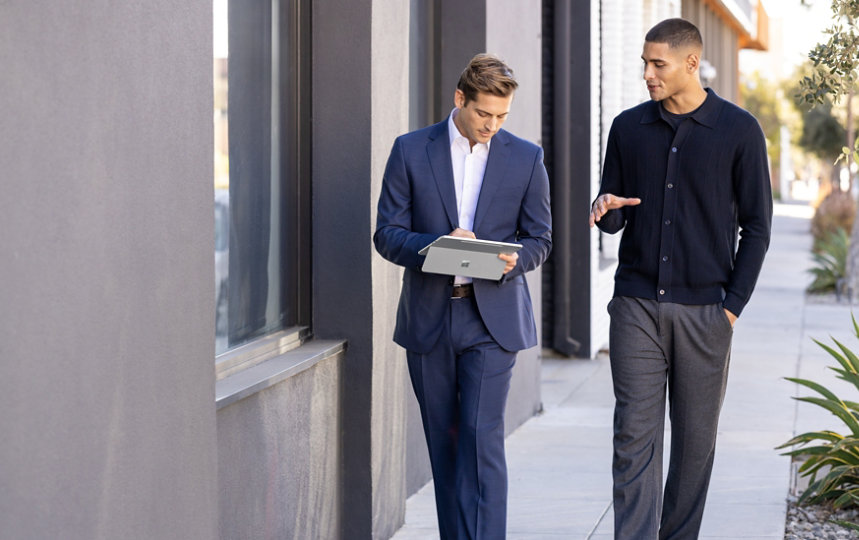 Two men with a tablet talking and walking outside on office campus