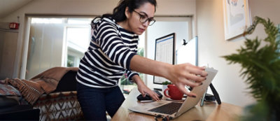 A woman in a striped shirt and glasses pointing at a laptop.