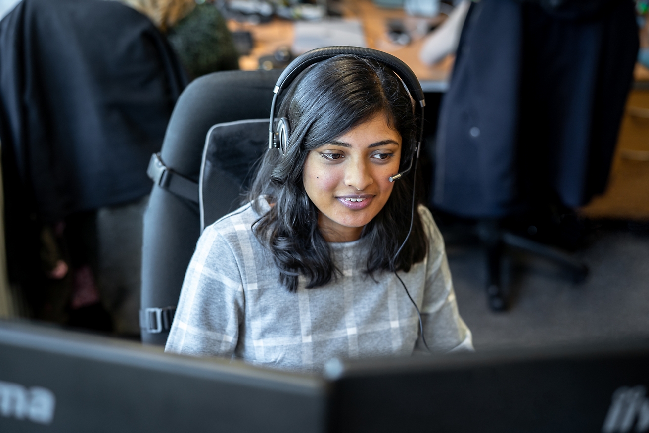En kvinne med et headset som arbeider på en datamaskin.
