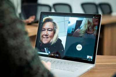 Persona che partecipa a una videochiamata sullo schermo di un portatile, con una donna che sorride nella finestra principale e un altro partecipante 