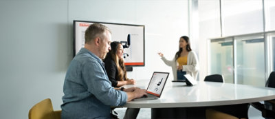 A person using a computer with two other persons in background