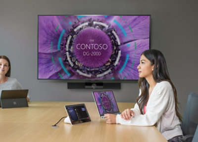 A woman sitting at a table looking at a laptop with the text CONTOSO DG-2000.