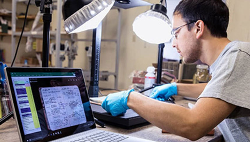 Mannelijke jongvolwassene zit in een lab waar hij een onderzoeksresultaat op een laptop verwerkt