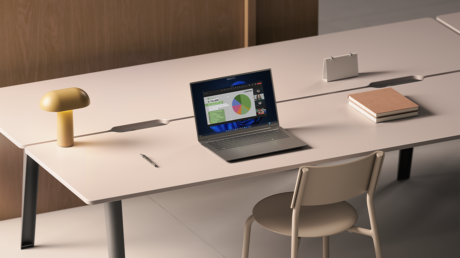 An open laptop displaying a shared screen on a video call sits on a long white desk alongside a lamp, pen, and books