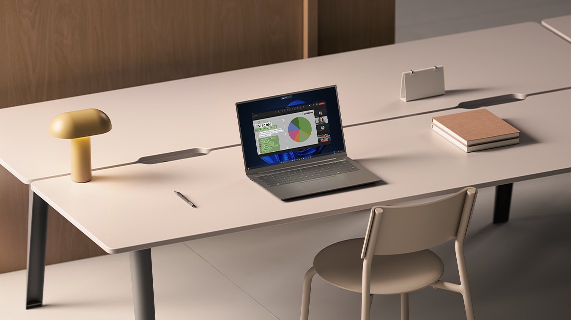 An open laptop displaying a shared screen on a video call sits on a long white desk alongside a lamp, pen, and books