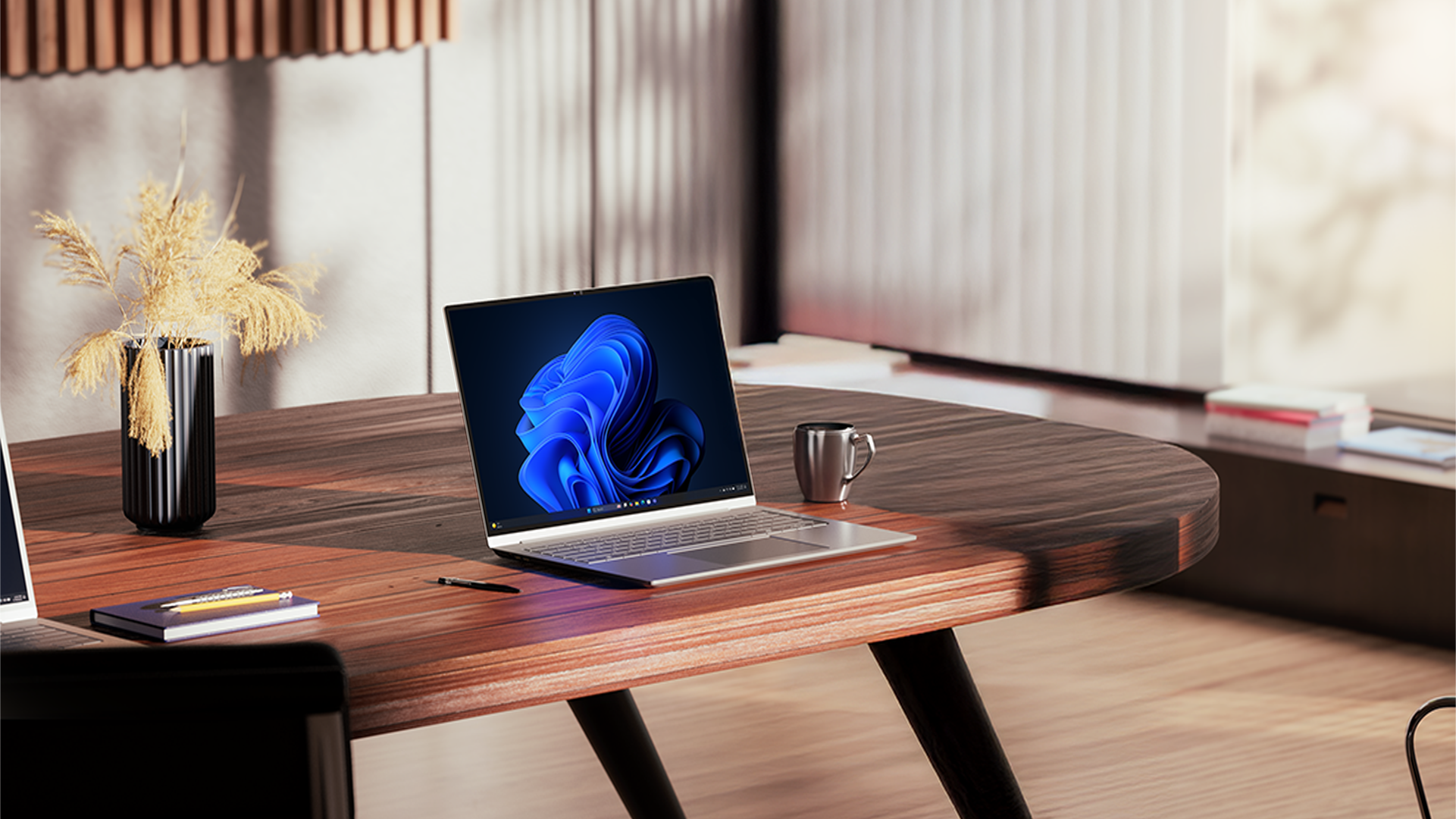 An open laptop displaying a Windows bloom background sits on a wooden desk in a well-lit office, alongside an espresso cup, vase of flowers, a notebook and pencils