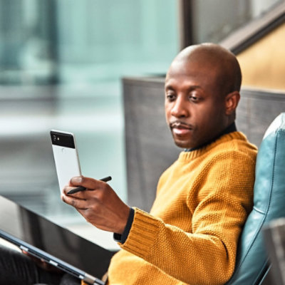 Personne assise sur un canapé. Elle tient un téléphone mobile à hauteur des yeux dans une main et une tablette dans l’autre main