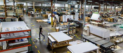 A man walks through a large, organized factory or warehouse with various equipment, materials