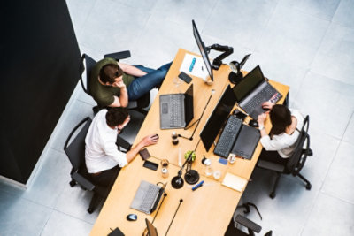 A top-down view of three people working at their desks with desktop monitors and laptops.