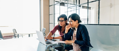 Due persone sedute alla scrivania dell'ufficio sono concentrate sullo schermo di un portatile.