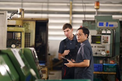 Two workers reviewing a tablet beside industrial machinery in a manufacturing facility.