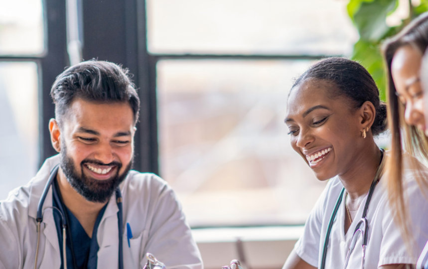 A small group of four medical professionals sit around a conference table as they meet to discuss patient cases