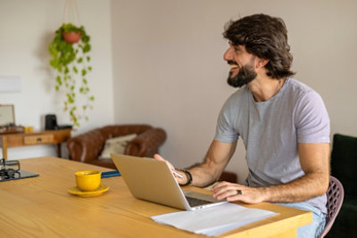 Young business man working at home in his kitchen with laptop and papers on kitchen wooden desk.
