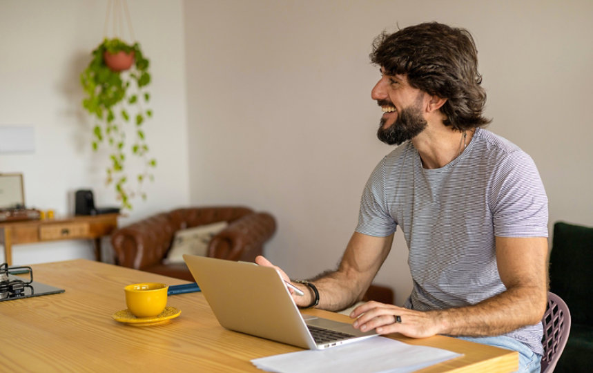 Young business man working at home in his kitchen with laptop and papers on kitchen wooden desk.