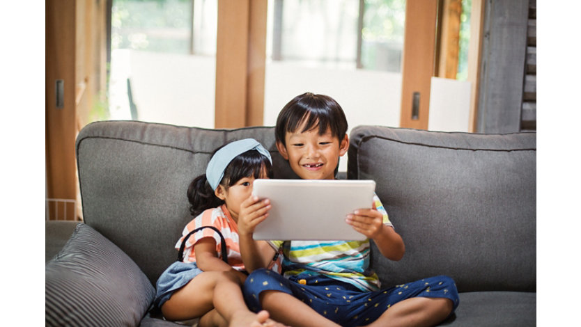 ソファに座ってタブレットで何かを見ている2人の子供