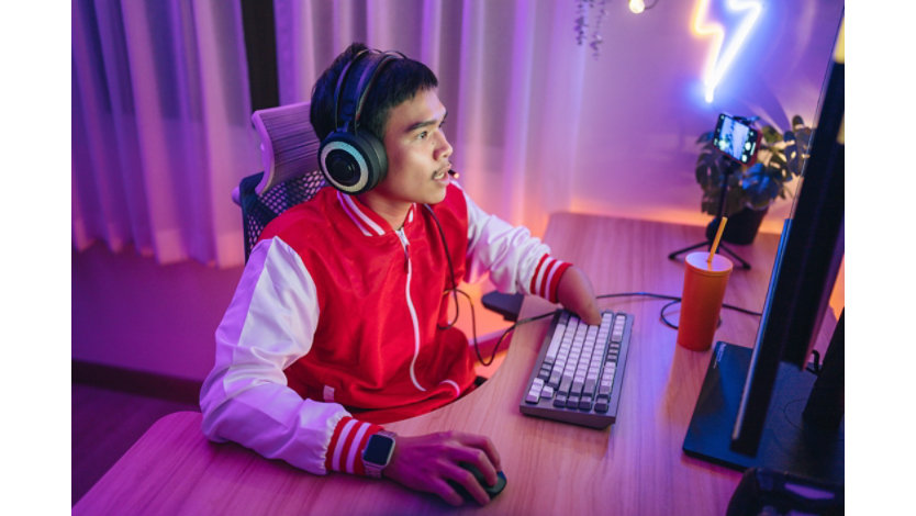 A disabled male gamer is wearing a headset and playing exciting online games in a neon-lit room.