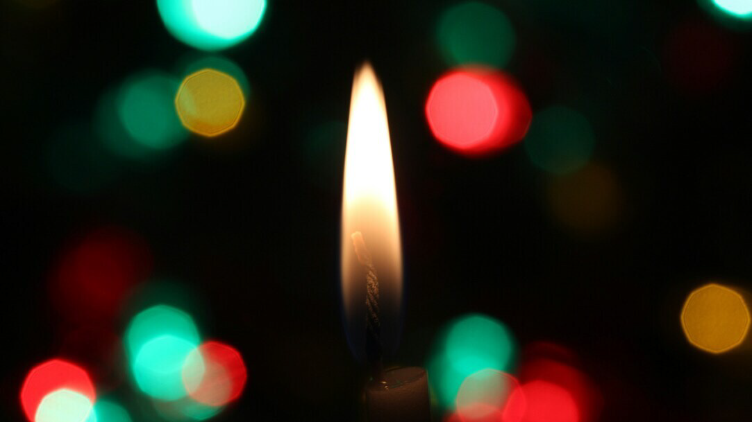 A candle flame against a dark backdrop with red and green and yellow light spots