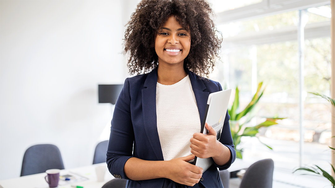 A confident young woman standing in an office and holding a clipboard
