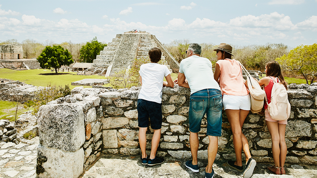 A family stands together taking in the view while exploring the ancient Mayapan ruins during their vacation