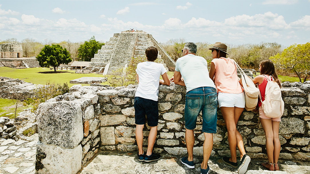 A family stands together taking in the view while exploring the ancient Mayapan ruins during their vacation