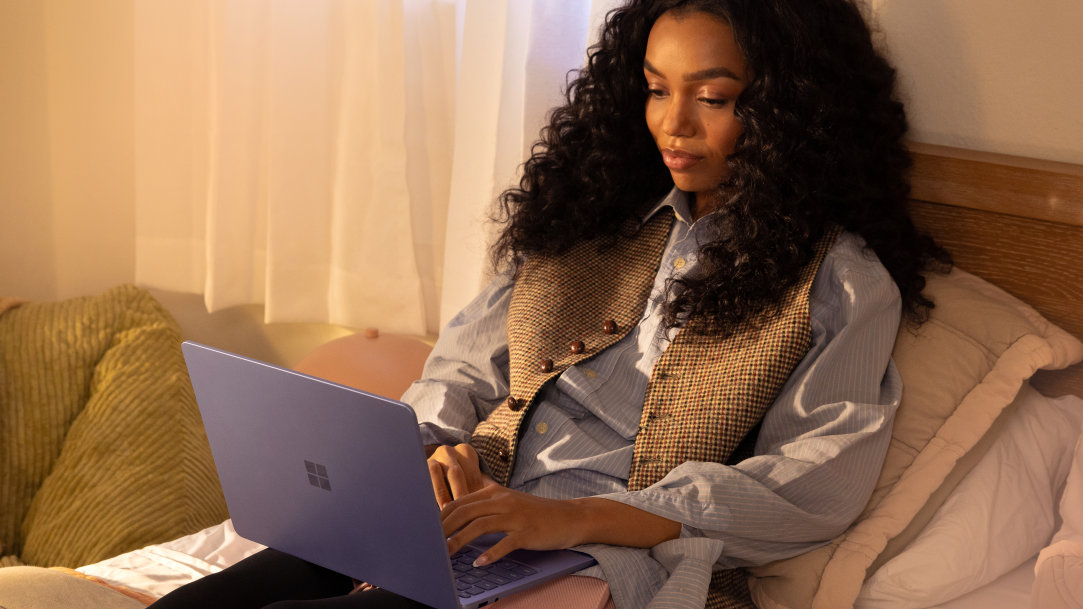 A female college student leaning against pillows and using a Surface Laptop Copilot+ PC