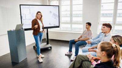 A female instructor in front of a small group of architecture students reviewing designs on a large screen