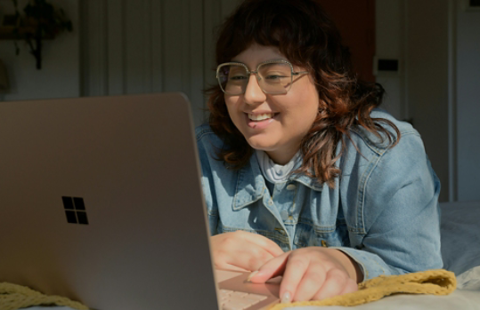 A girl who’s smiling and using a gold Surface laptop