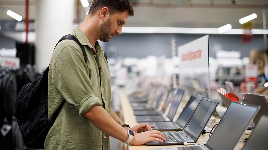 A male consumer comparing laptops in a retail computer store