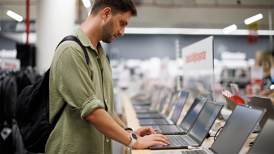 A male consumer comparing laptops in a retail computer store