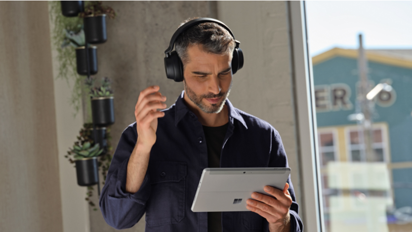 A man holding a Surface and wearing headphones