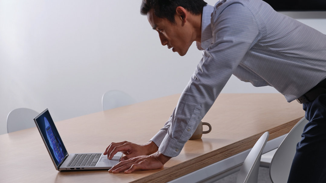 Un hombre se inclina sobre una mesa mientras usa un portátil.