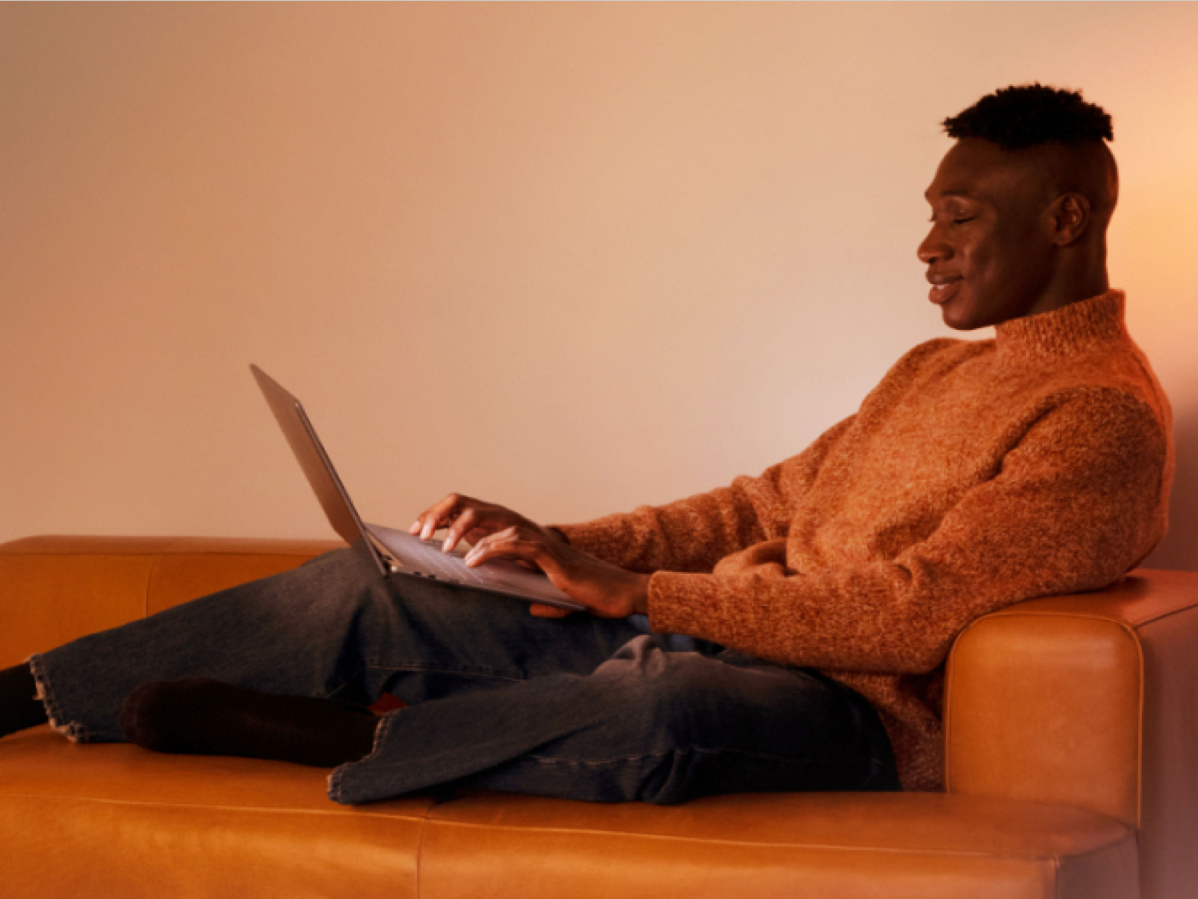 Un hombre relajándose sobre un sofá naranja y usando su portátil