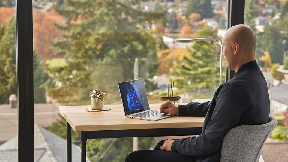 A man sits at his home office desk. The start screen of a Surface Laptop Go 2 is observed.