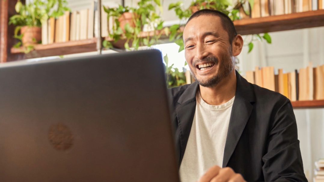 A man smiling and sitting at a table looking at his computer